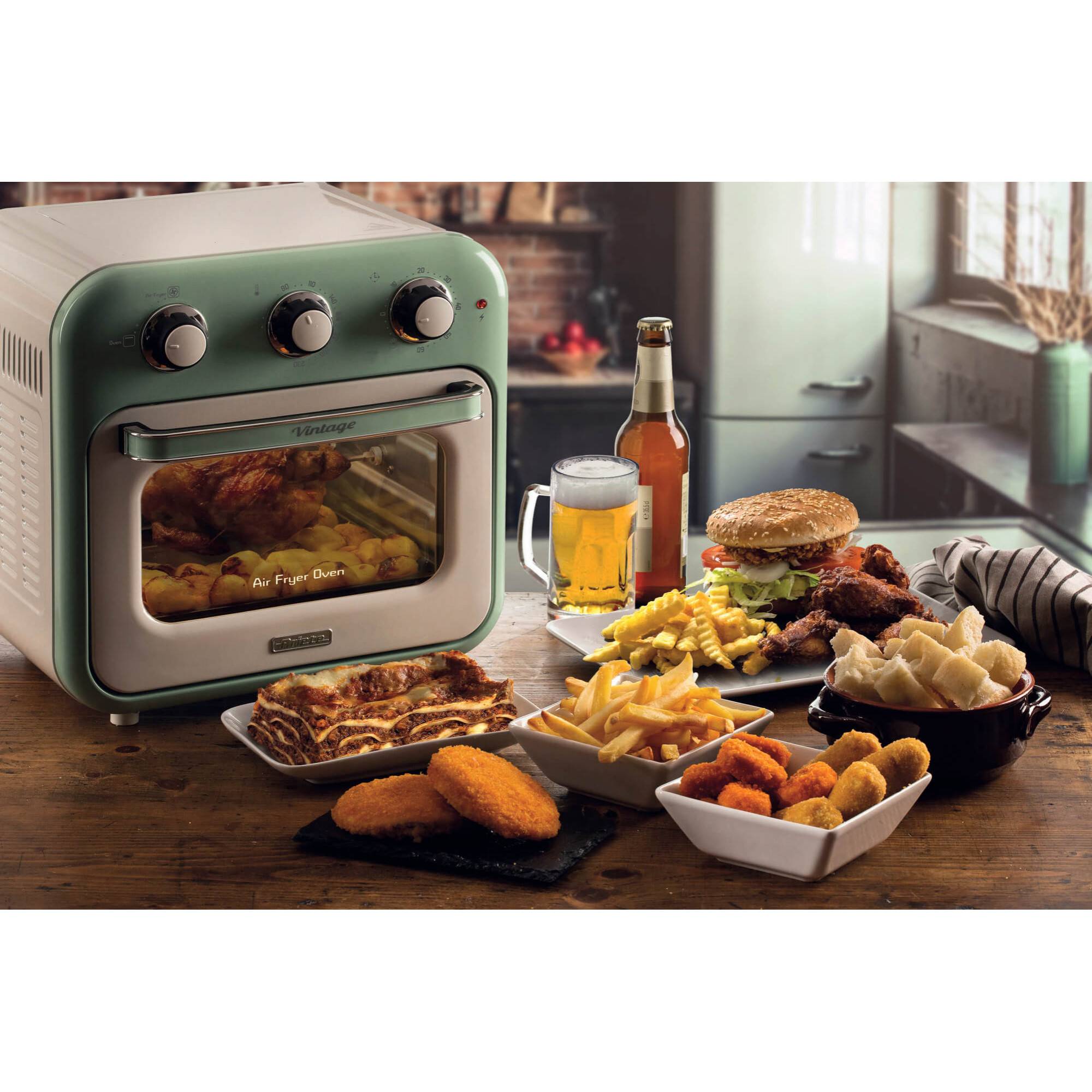 Friteuse auf einer Küchenarbeitsplatte neben einem Bier und einer Auswahl von Frittiertem, einem Burger, Pommes und Snacks auf Tellern