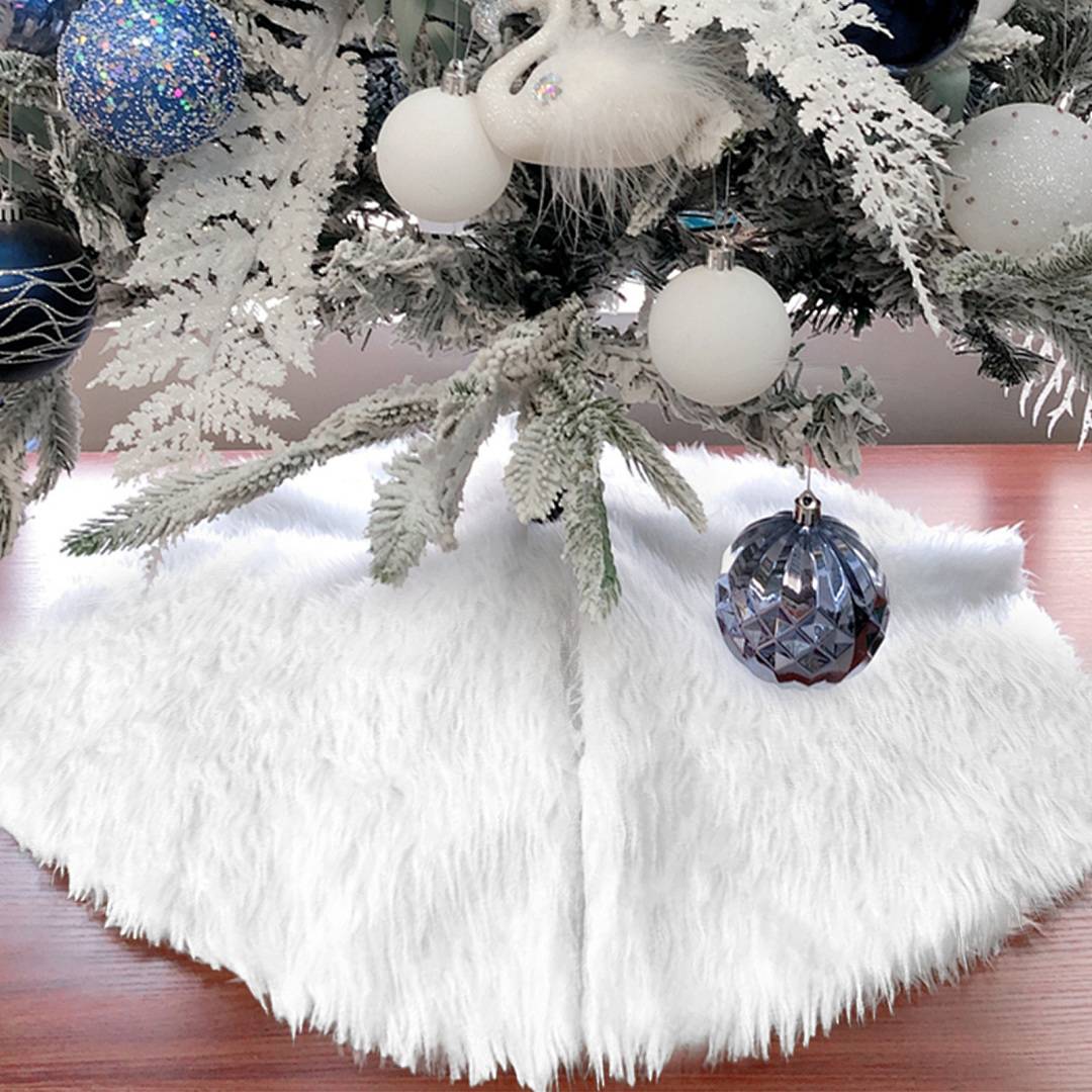 Boden eines dekorierten Weihnachtsbaums mit weißem Kunstfellbaumrock und hängenden silbernen, blauen und weißen Kugeln auf einem Holzboden.