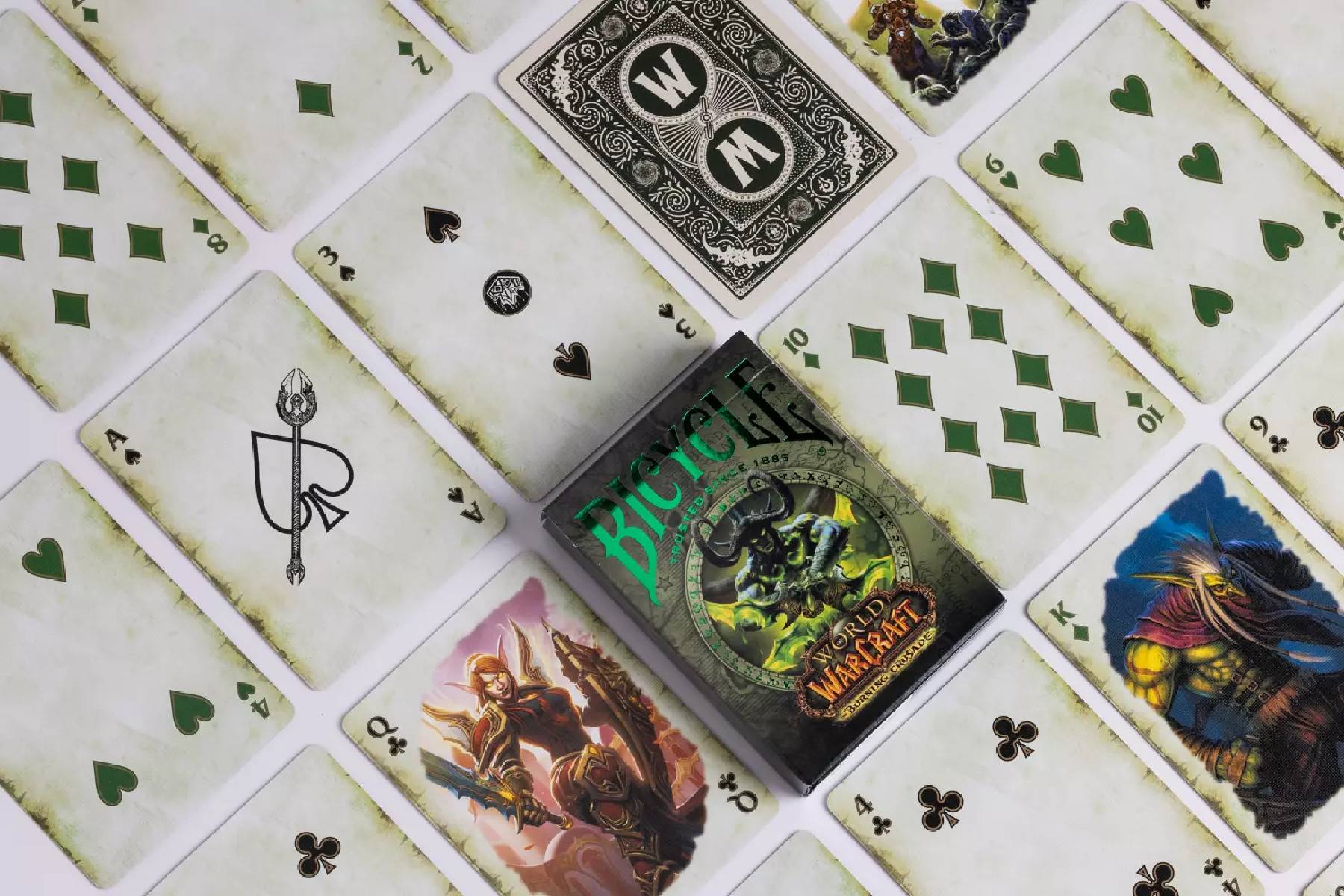 Ein verpacktes 'World of Warcraft' Sammelkartenspiel-Pack liegt zwischen verstreuten Spielkarten mit verschiedenen Farben und Illustrationen von Hofkarten.