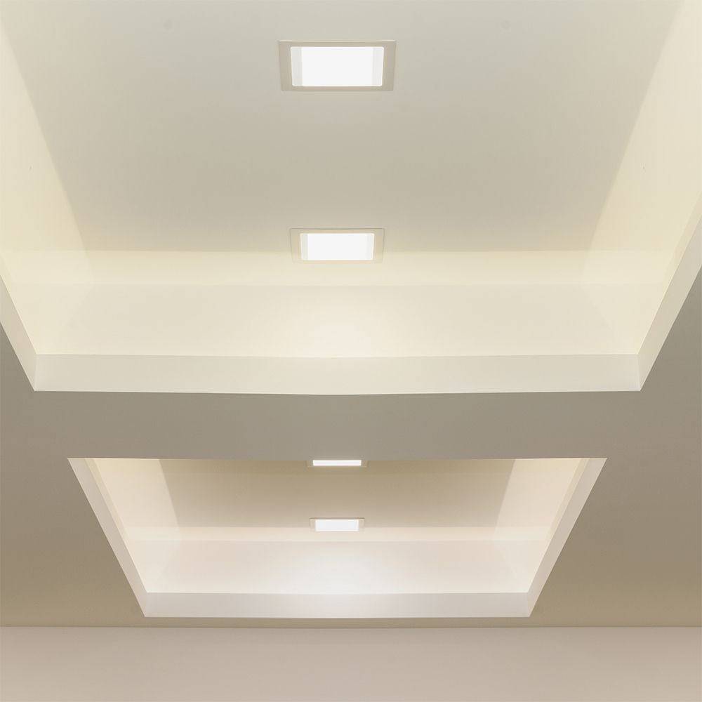 Eine moderne Decke mit zwei eingelassenen Beleuchtungspaneelen, die saubere Linien und ein minimalistisches Design aufweisen und weiches Licht in einen neutralen Raum werfen.