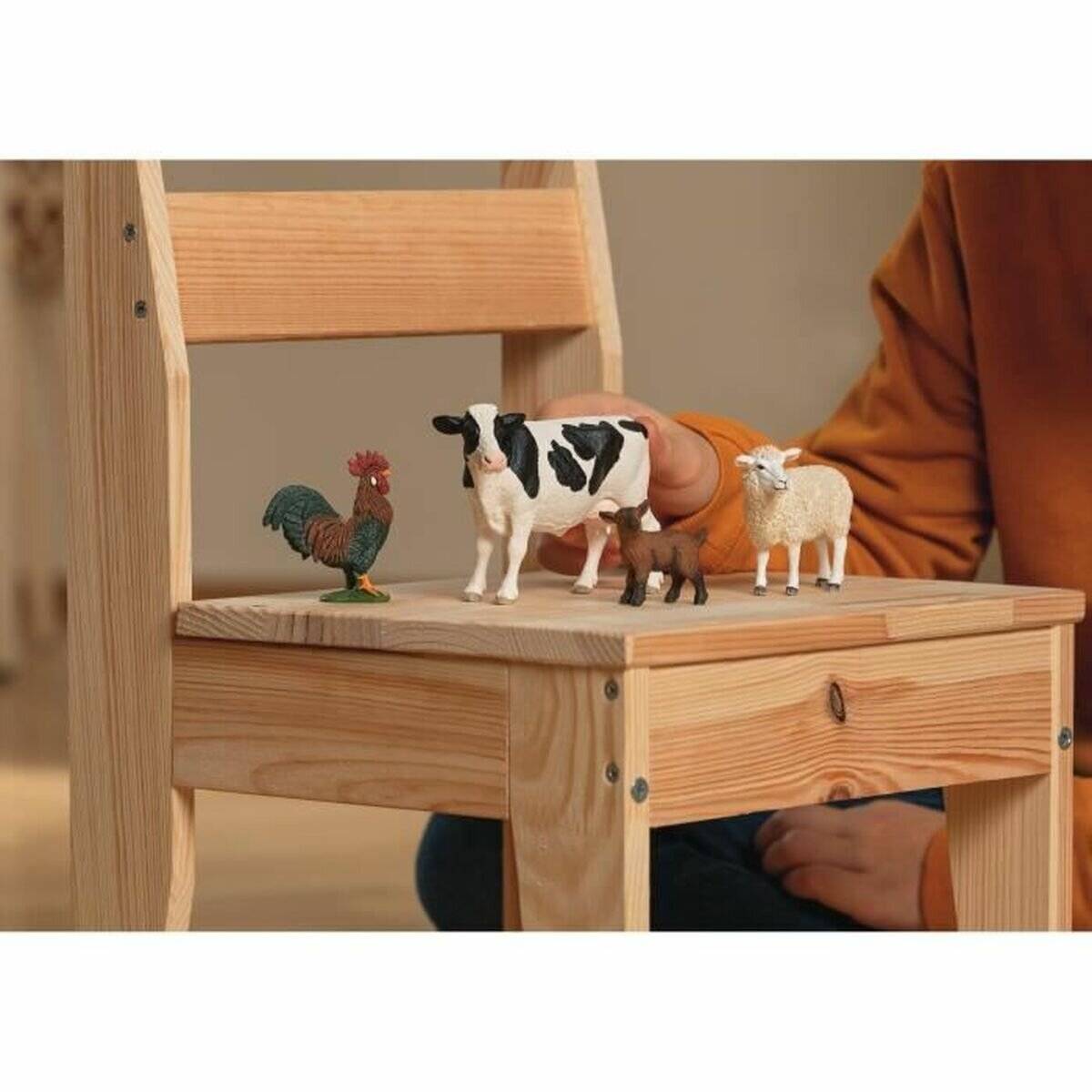 Ein Kind ordnet Spielzeugfarmatiere auf einem Holzstuhl an: einen Hahn, eine Kuh, ein Pferd und ein Schaf.