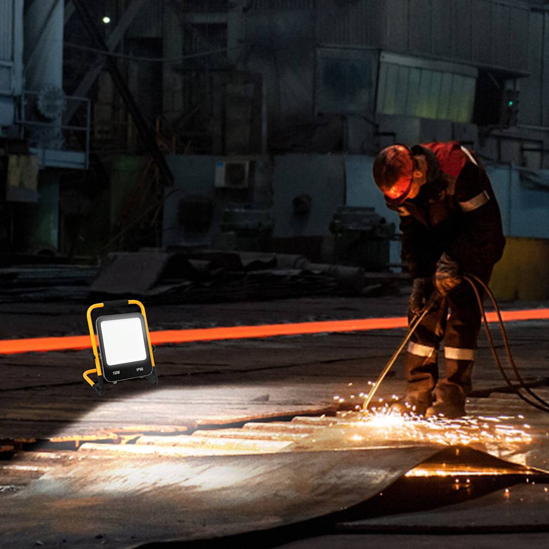 Ein Arbeiter, der eine Schweißflamme in einer Industriewerkstatt benutzt, mit Funken, die über den Boden fliegen, und einer tragbaren Arbeitsleuchte in der Nähe.