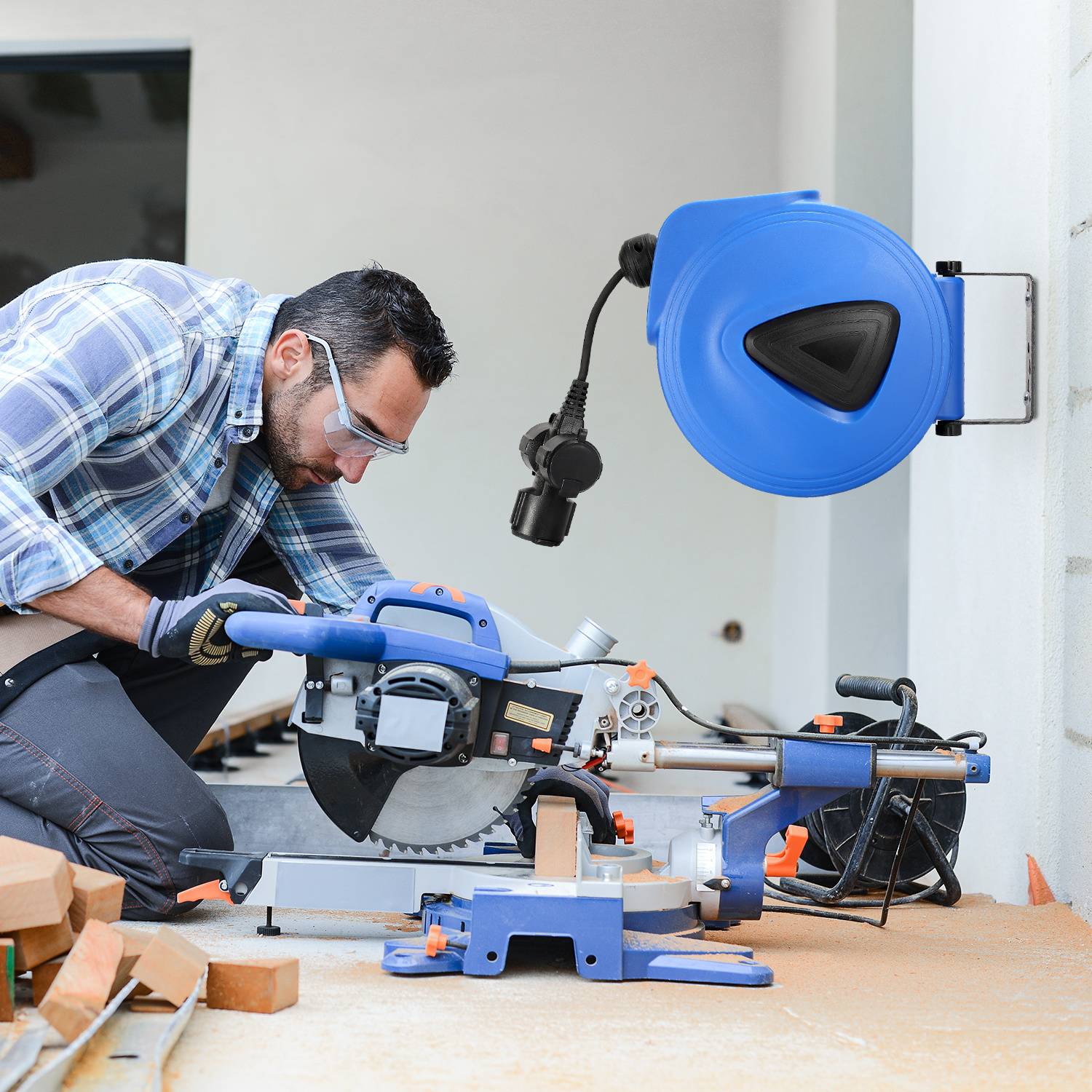 Ein Mann, der eine Schutzbrille trägt, benutzt eine Gehrungssäge an Holz in Innenräumen, während eine an der Wand montierte blaue ausziehbare Schlauchrolle in der Nähe steht.