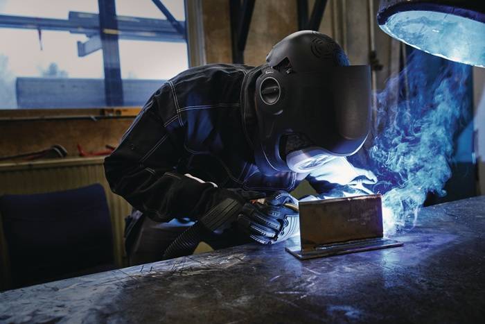 Ein Schweißer mit Schutzausrüstung schweißt Metall im Innenbereich und erzeugt helle Funken in einer Werkstattumgebung.