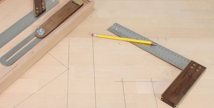 Ein Holztisch mit einem Metalllineal, einem gelben Bleistift und einer Holzkiste. Auf dem Tisch sind Pläne skizziert, die auf ein Tischlereiprojekt hindeuten.