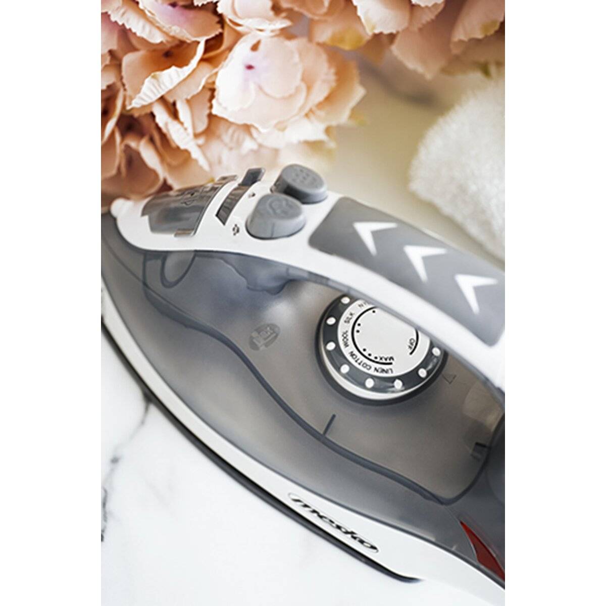 Nahaufnahme eines weiß-grauen Dampfbügeleisens auf einer Marmoroberfläche mit zarten rosa Blüten im Hintergrund.