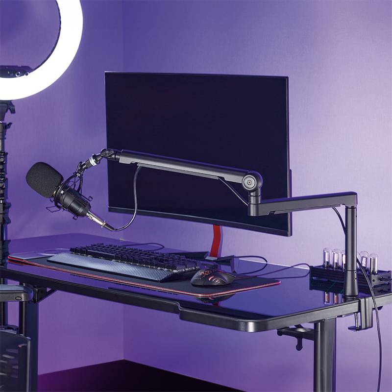 Ein moderner Arbeitsplatz mit einem großen Monitor, Tastatur, Maus, Mikrofon auf einem verstellbaren Arm und einem Ringlicht auf einem eleganten schwarzen Schreibtisch.