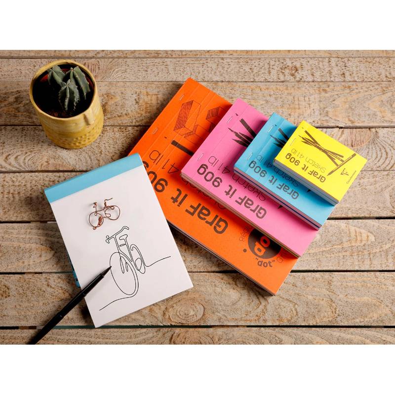 Verschiedenfarbige Notizbücher, eines mit einer Fahrradzeichnung, sind auf einer Holzoberfläche angeordnet. Ein kleiner Kaktus in einem Topf steht in der Nähe.