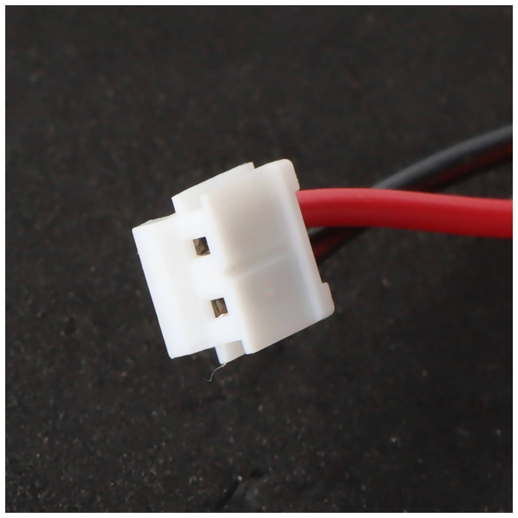 Nahaufnahme eines weißen zweipoligen Elektrosteckers, der an roten Drähten auf dunklem Hintergrund angebracht ist.