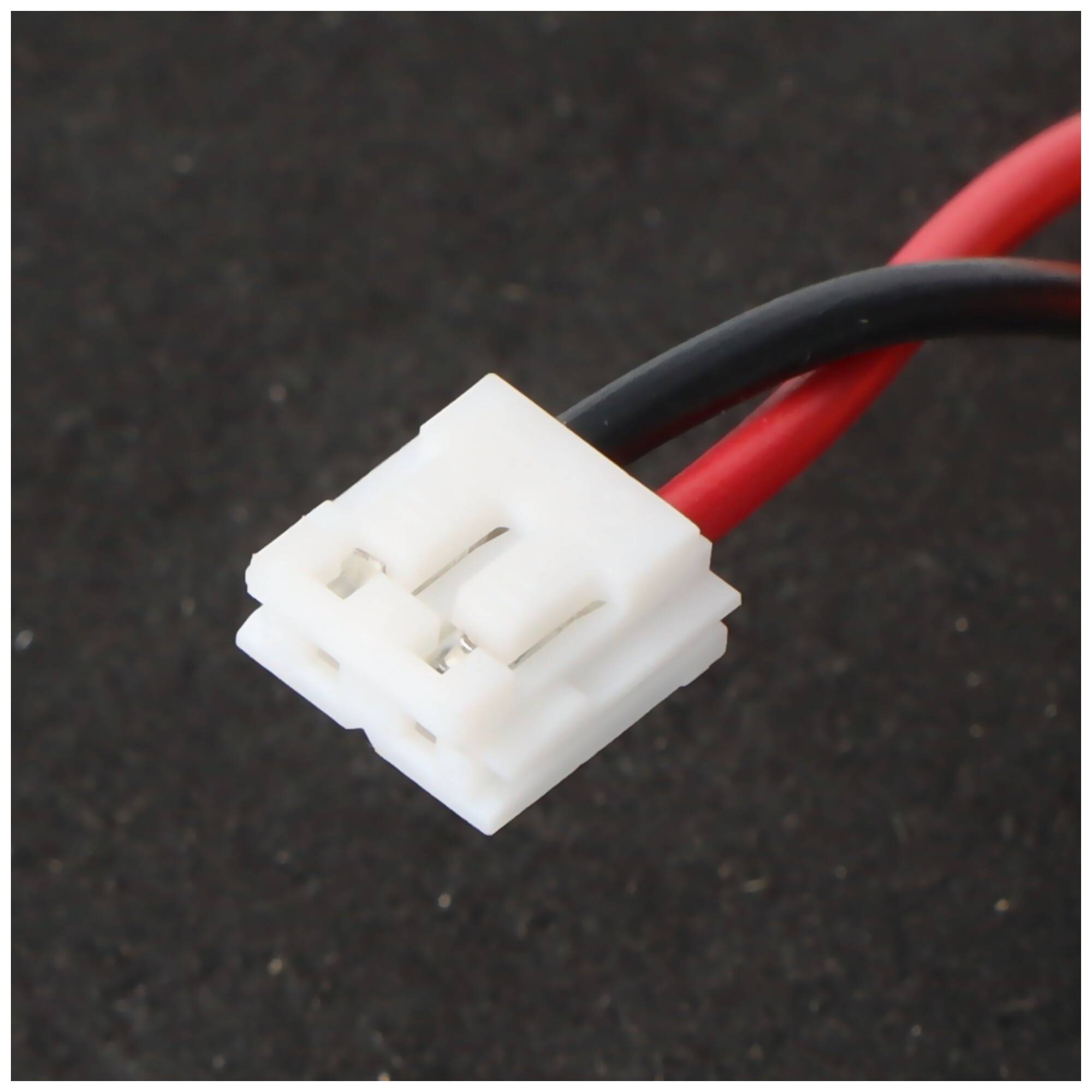 Nahaufnahme eines weißen zweipoligen Elektrosteckers, der an roten und schwarzen Drähten auf dunklem Hintergrund befestigt ist.