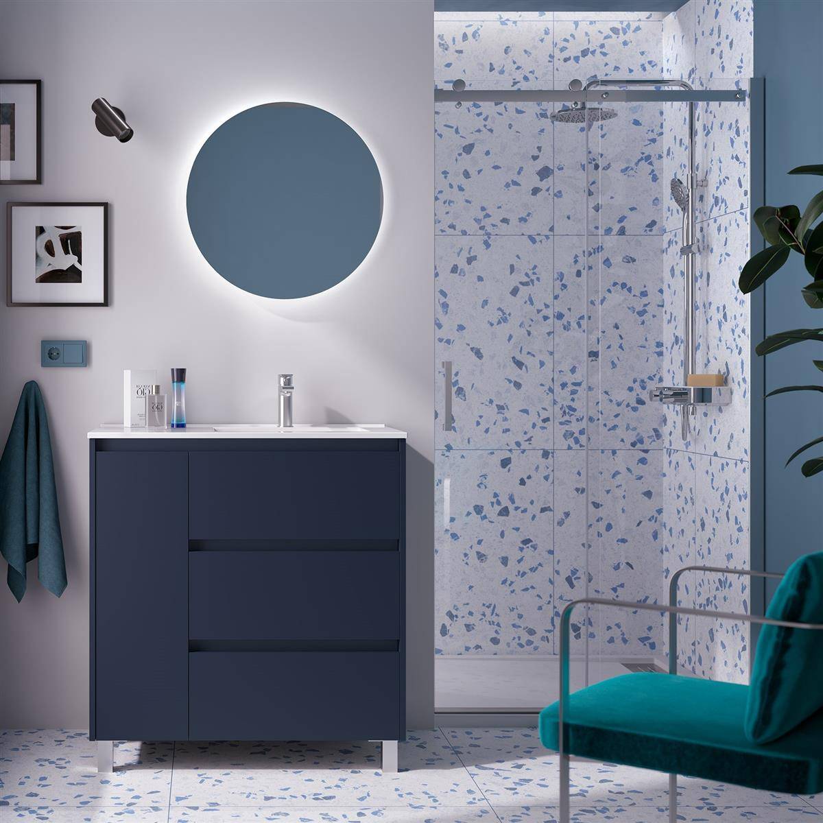 Modernes Badezimmer mit marineblauem Waschbeckenunterschrank und rundem blauem Spiegel, Glasdusche mit gesprenkeltem Fliesenbelag, Tealstuhl und Tealhandt­uchakzenten.
