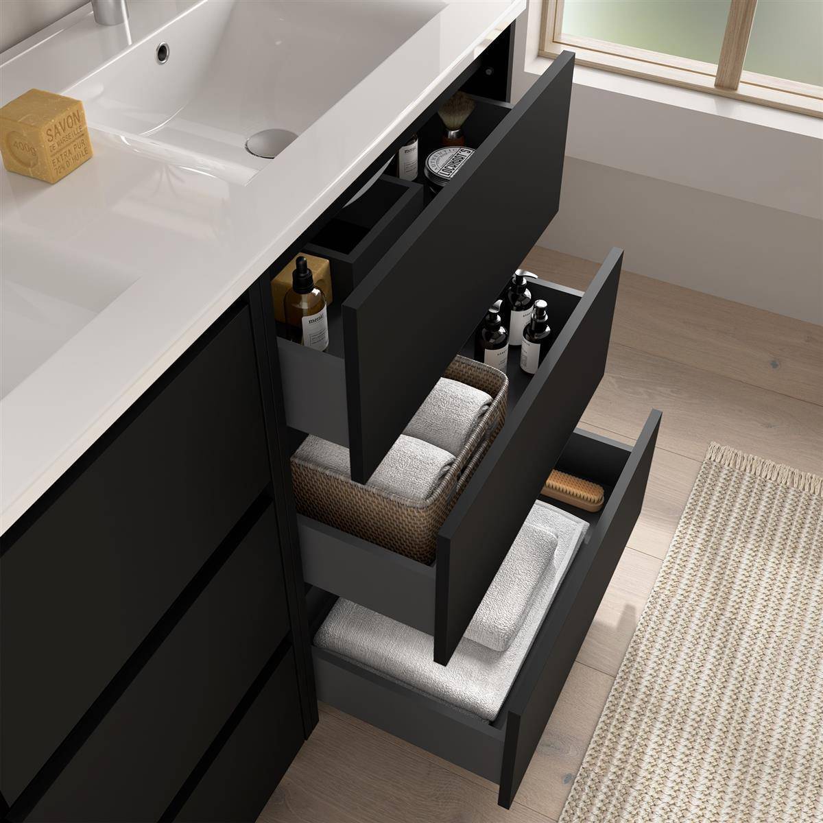 Badezimmerschrank mit drei offenen Schubladen, in denen Toilettenartikel, Handtücher und Aufbewahrungskörbe neben einem Waschbecken ordentlich angeordnet sind.