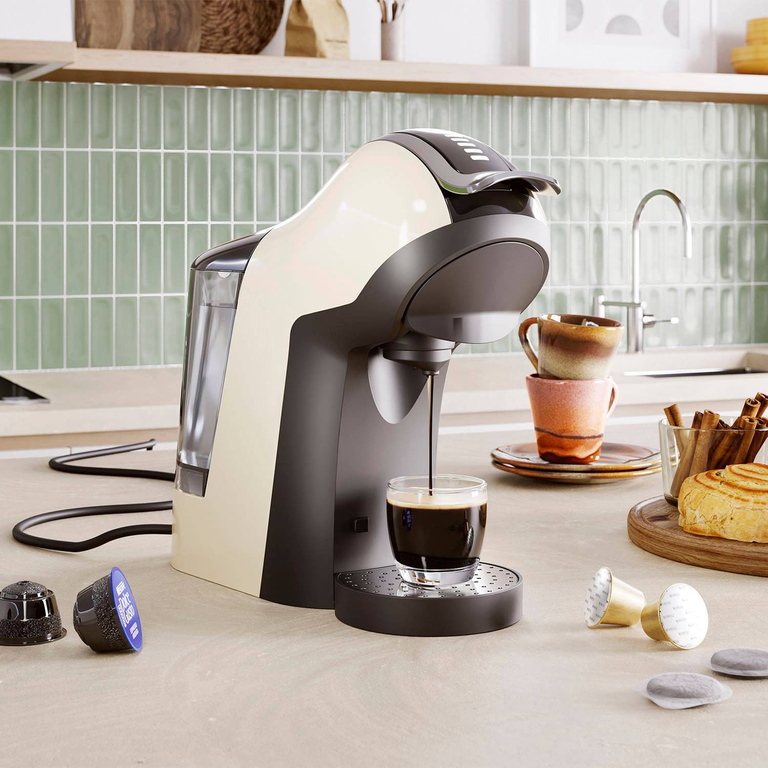 Eine Kaffeemaschine auf einer Küchenarbeitsplatte brüht eine Tasse Espresso. In der Nähe sind Kaffeekapseln und ein Gebäck arrangiert, mit einer gefliesten Rückwand und einem Wasserhahn im Hintergrund.
