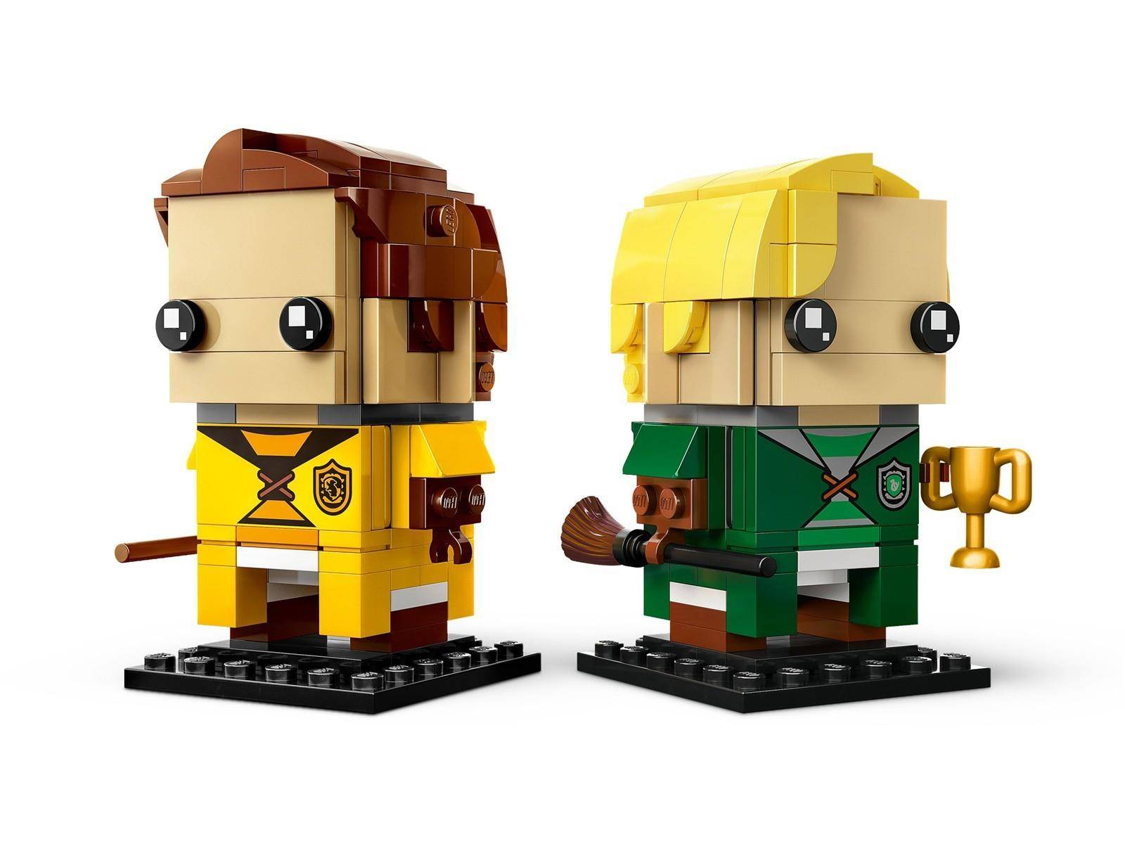 Zwei LEGO-ähnliche Harry-Potter-Minifiguren auf Ständern: eine in Gelb mit braunem Haar, eine in Grün mit blondem Haar, die einen Pokal hält.