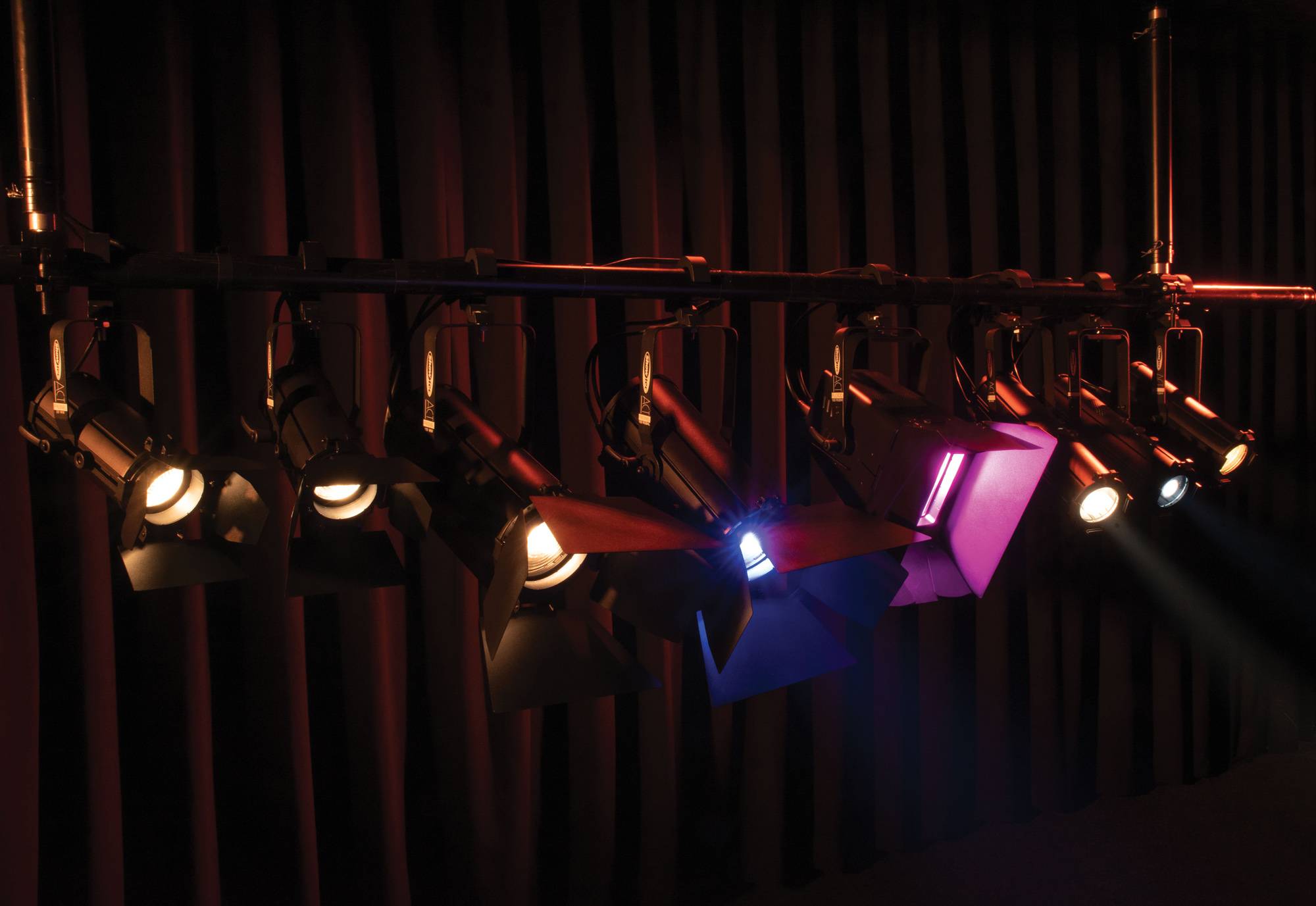 Bühnenlichter in einer Reihe werfen farbige Lichtstrahlen auf eine dunkle Bühne und schaffen eine dramatische Atmosphäre.