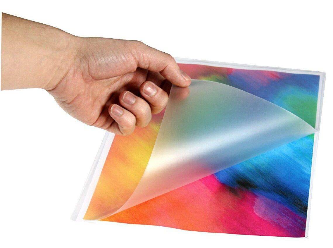 Eine Hand, die eine durchsichtige Folie von einem farbig bedruckten Blatt zurückzieht und das glänzende Bild darunter enthüllt.