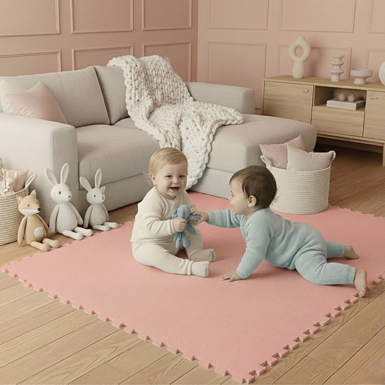 Zwei Kleinkinder sitzen auf einer rosa Matte in einem gemütlichen Wohnzimmer, umgeben von Plüschtieren. Ein Kind reicht dem anderen ein weiches Spielzeug und lächelt.