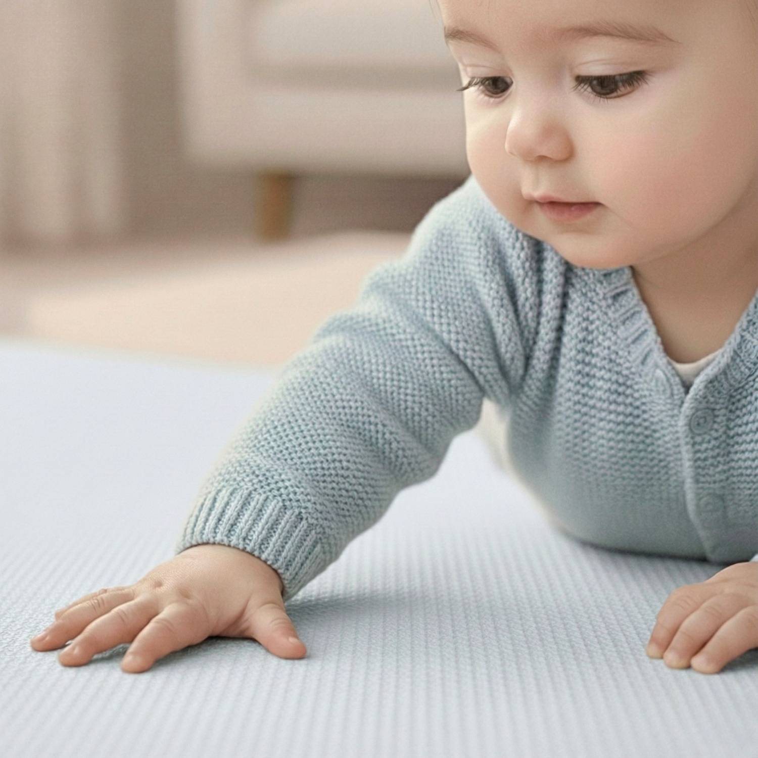 Ein Baby mit einem hellblauen Pullover krabbelt auf einer weichen, neutralfarbenen Oberfläche und ist konzentriert nach vorne gerichtet in einer gemütlichen Inneneinrichtung.