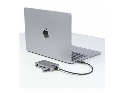 Ein silberner Laptop ist an einem USB-C-Multi-Port-Hub auf einer weißen Oberfläche angeschlossen. Der Hub verfügt über mehrere Anschlüsse für die Konnektivität.