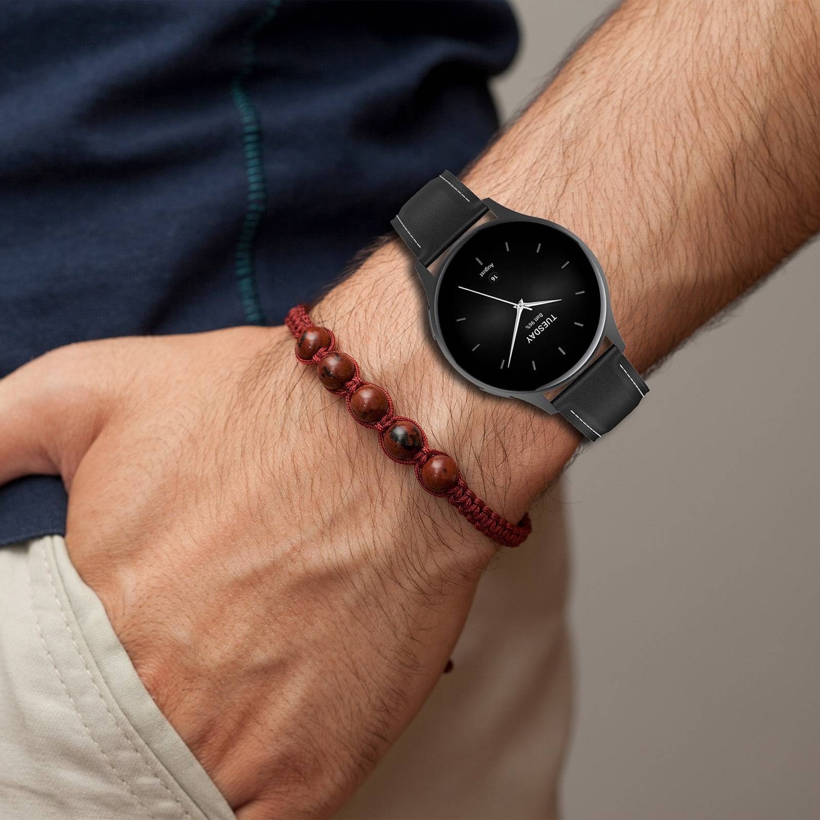Nahaufnahme eines Handgelenks mit einer schwarzen Analoguhr und einem braunen Perlenarmband.