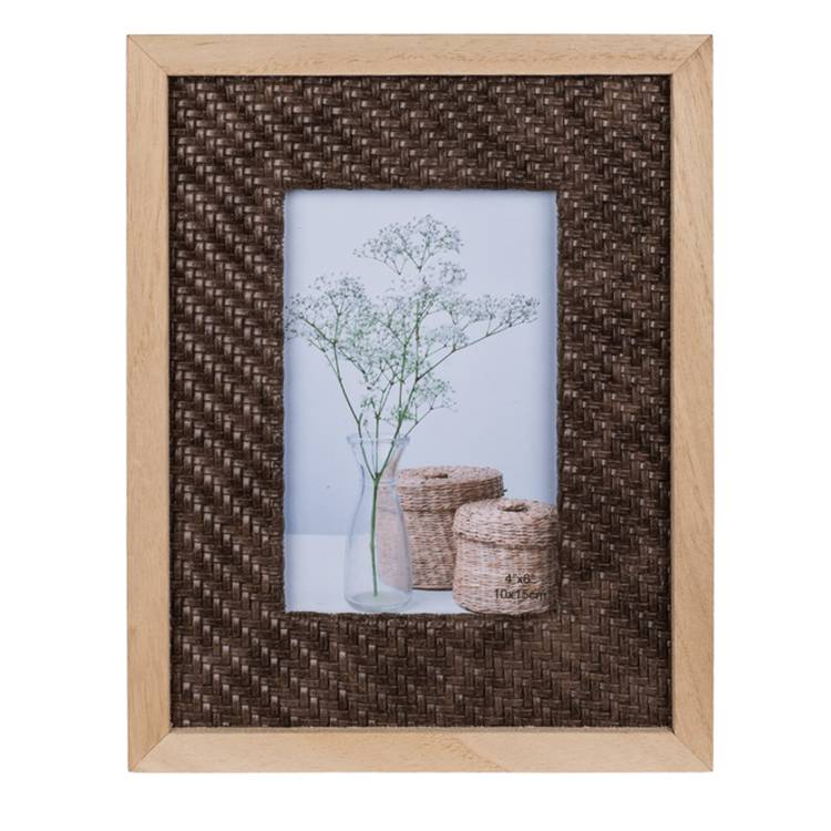 Ein gerahmtes Bild zeigt eine zarte Pflanze in einer Vase neben zwei kleinen geflochtenen Körben auf einer ebenen Oberfläche vor einem weißen Hintergrund.