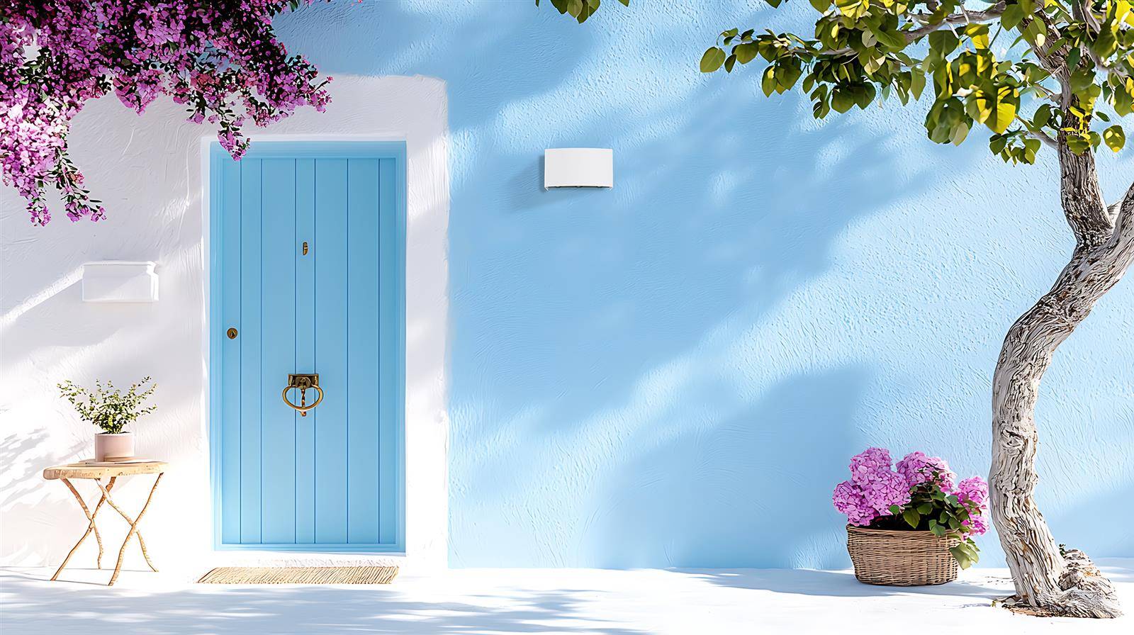 Strahlend blaugraue Hausfassade mit einer hellblauen Tür, Topfblumen und einem Baum, der Schatten auf einem sonnigen Innenhof wirft.