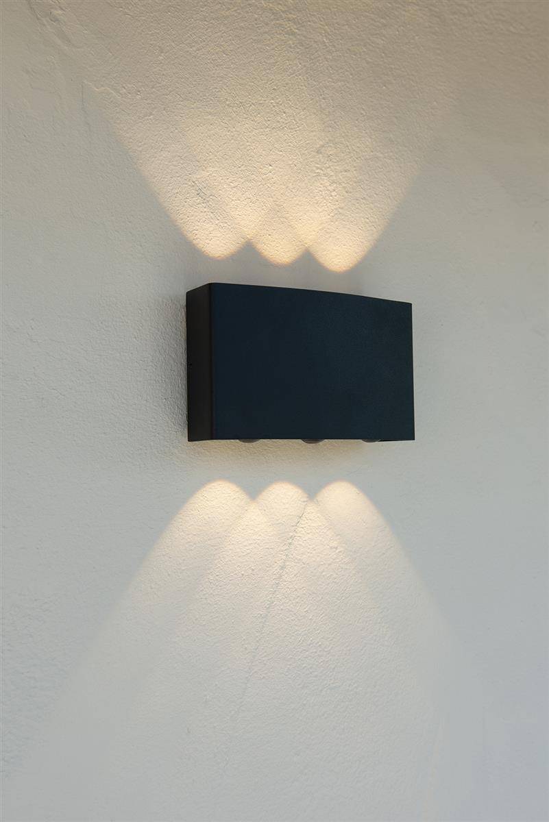Schwarze rechteckige Wandleuchte an einer hellen Wand, die symmetrische Licht- und Schattenstrahlen in warmer Farbe wirft.