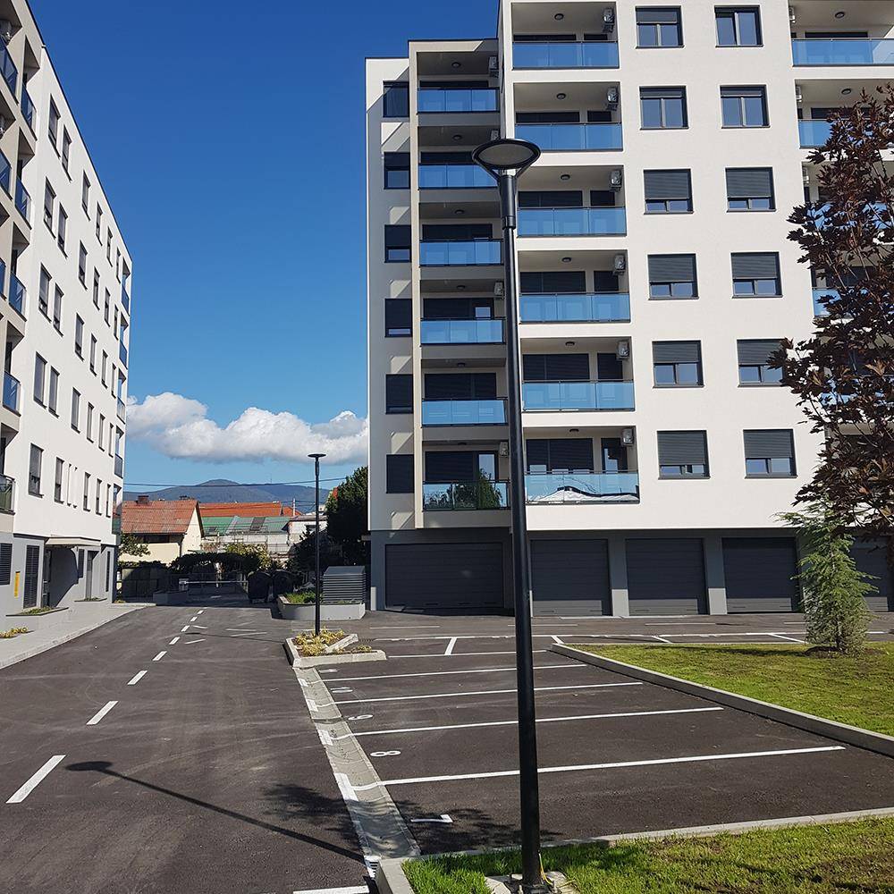 Eine ruhige Wohnstraße mit modernen Mehrfamilienhäusern, leeren Parkplätzen und einem klaren blauen Himmel, was auf einen friedlichen Stadtteil hindeutet.