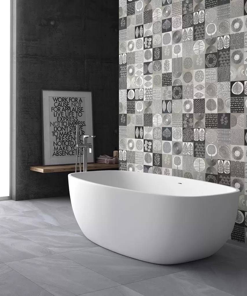 Modernes Badezimmer mit einer freistehenden weißen ovalen Badewanne neben einer gemusterten Fliesenschmuckwand und einem Motivationsspruch in einem Rahmen an einer dunklen Wand.