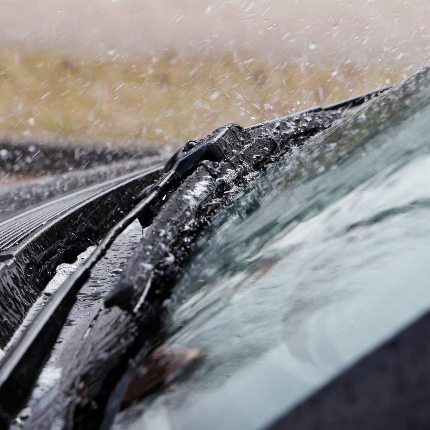 Eine Nahaufnahme von Scheibenwischern im Einsatz während eines Regensturms, die Regentropfen von der Windschutzscheibe eines Autos wischen, um die Sicht zu verbessern.