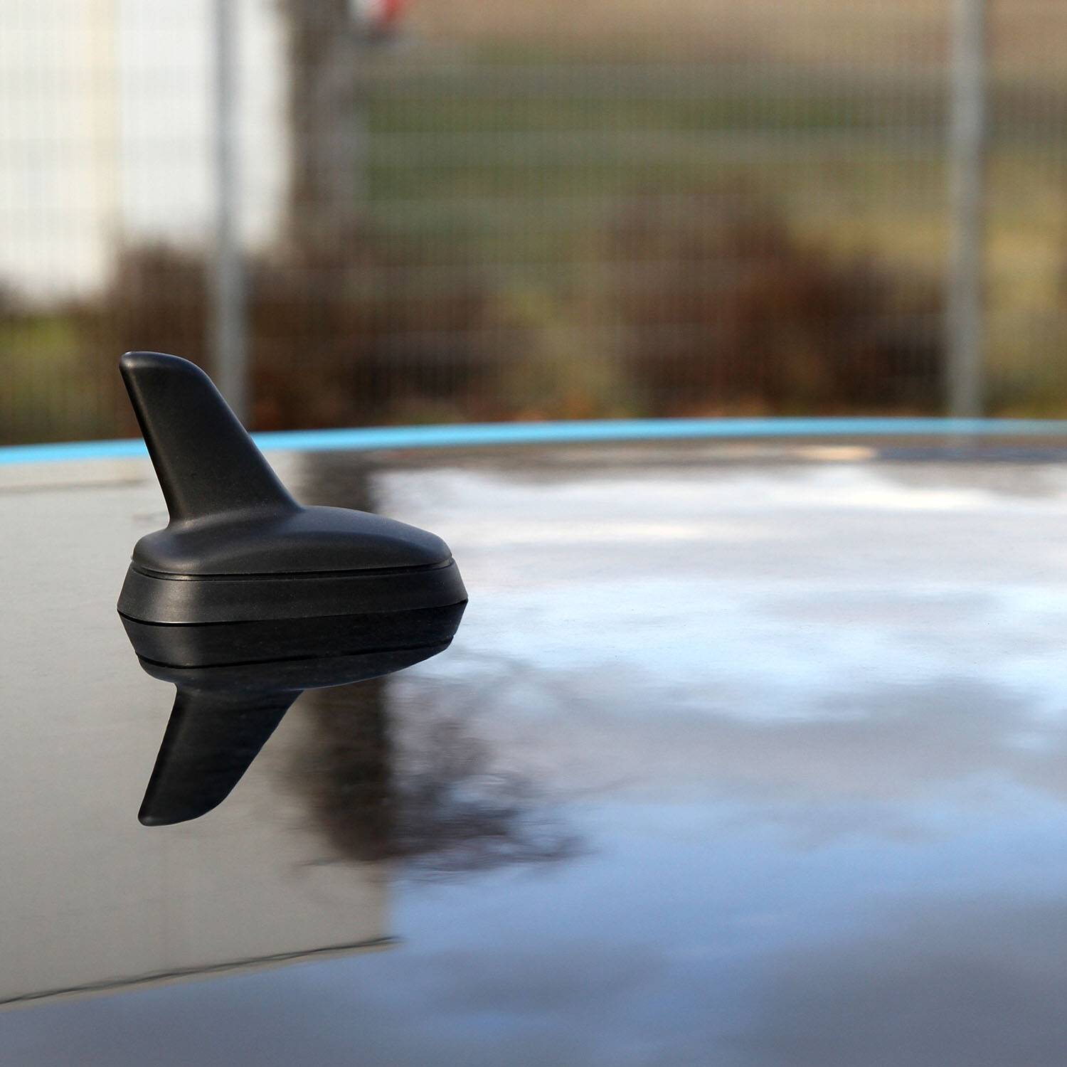 Eine schwarze Haifischflossen-Antenne ist auf dem Dach eines Autos montiert und spiegelt ihre schlanke Form gegen einen unscharfen Außenhintergrund.
