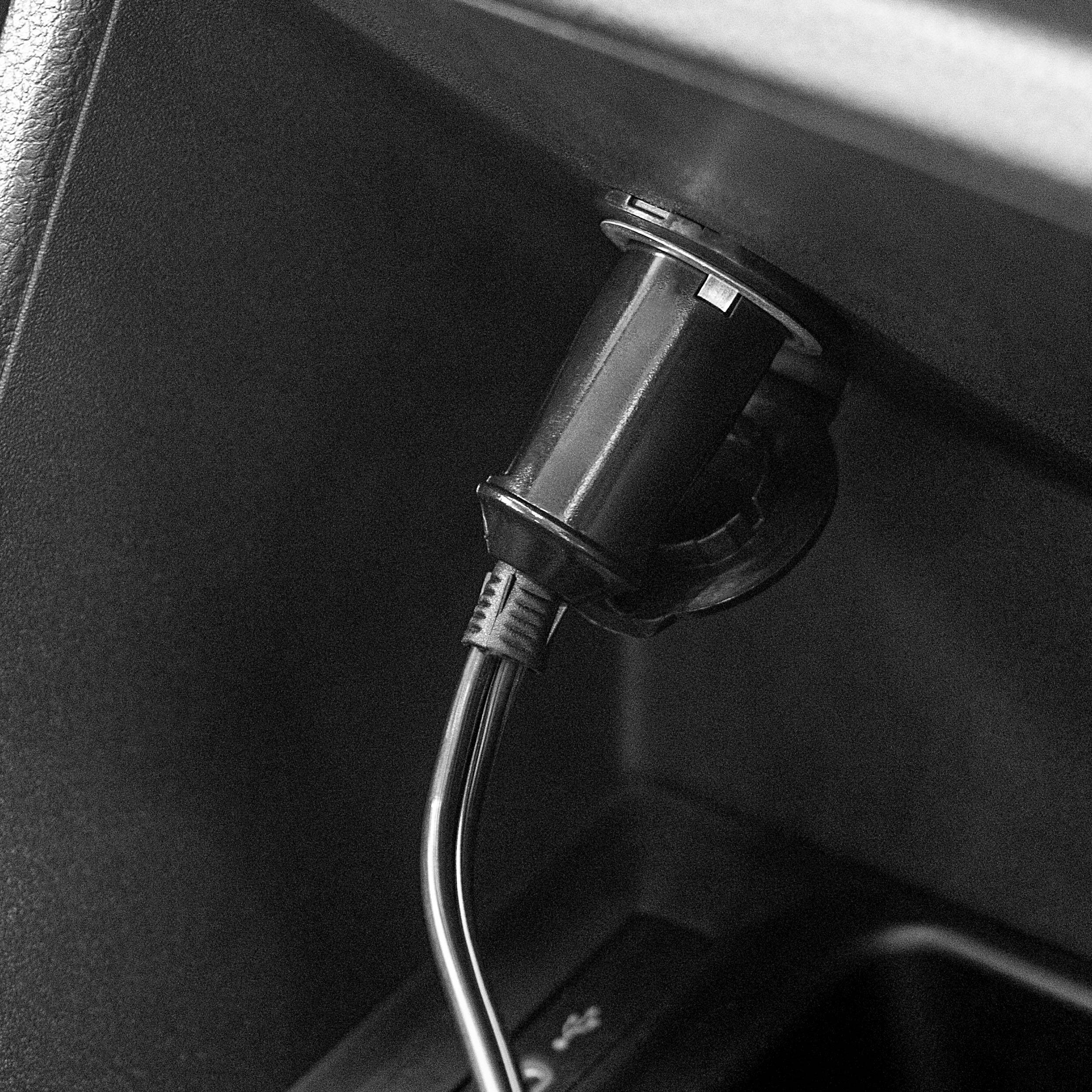 Nahaufnahme des 12-V-Zigarettenanzünder-Stromauslasses eines Autos mit einem eingesteckten Ladegerät und sichtbarem USB-Kabel in der Mittelkonsole.