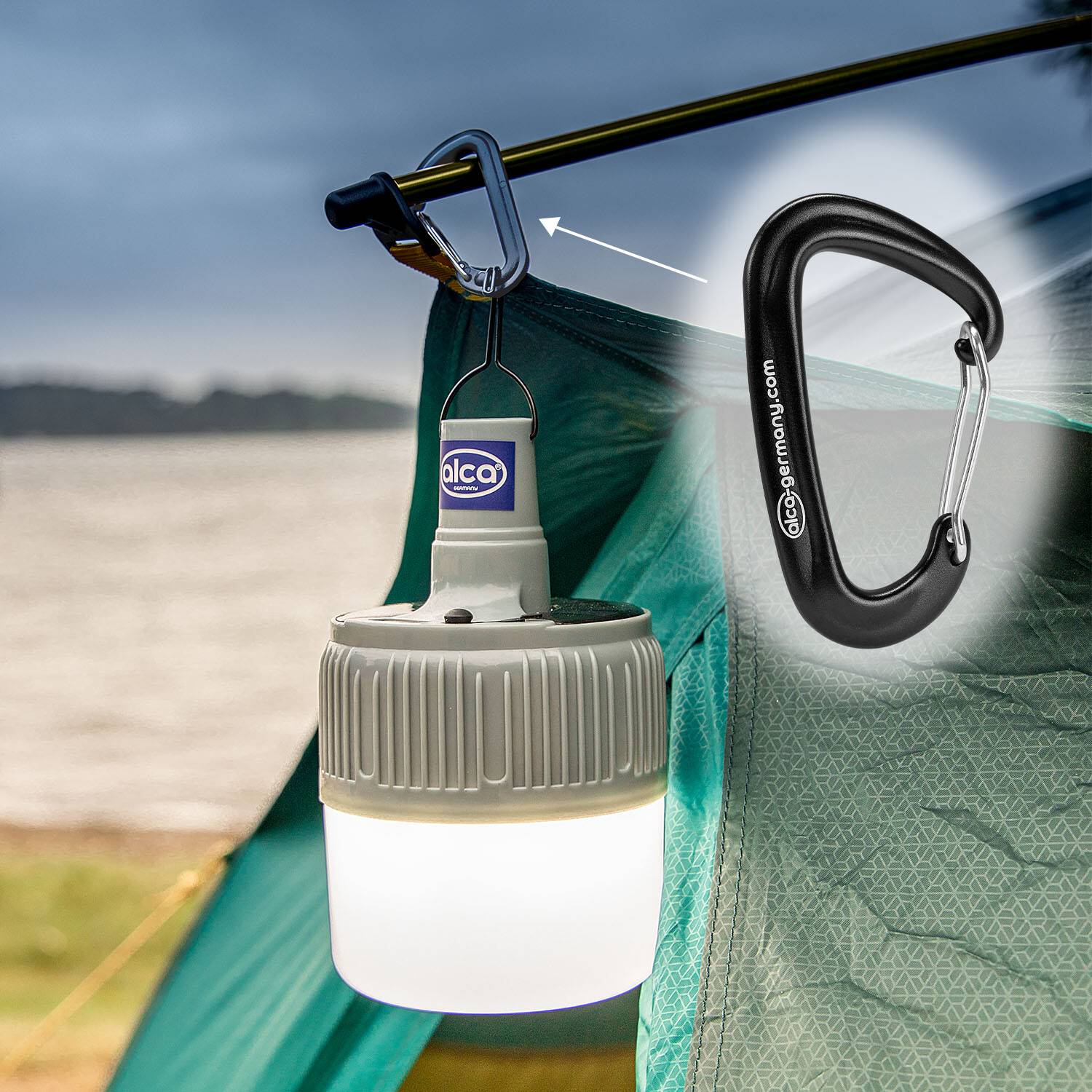 Campinglaterne, die mit einem Karabiner an der Innenseite eines Zeltes aufgehängt ist. Eine Nahaufnahme des Karabiners ist zu sehen, mit einem See im Hintergrund sichtbar.