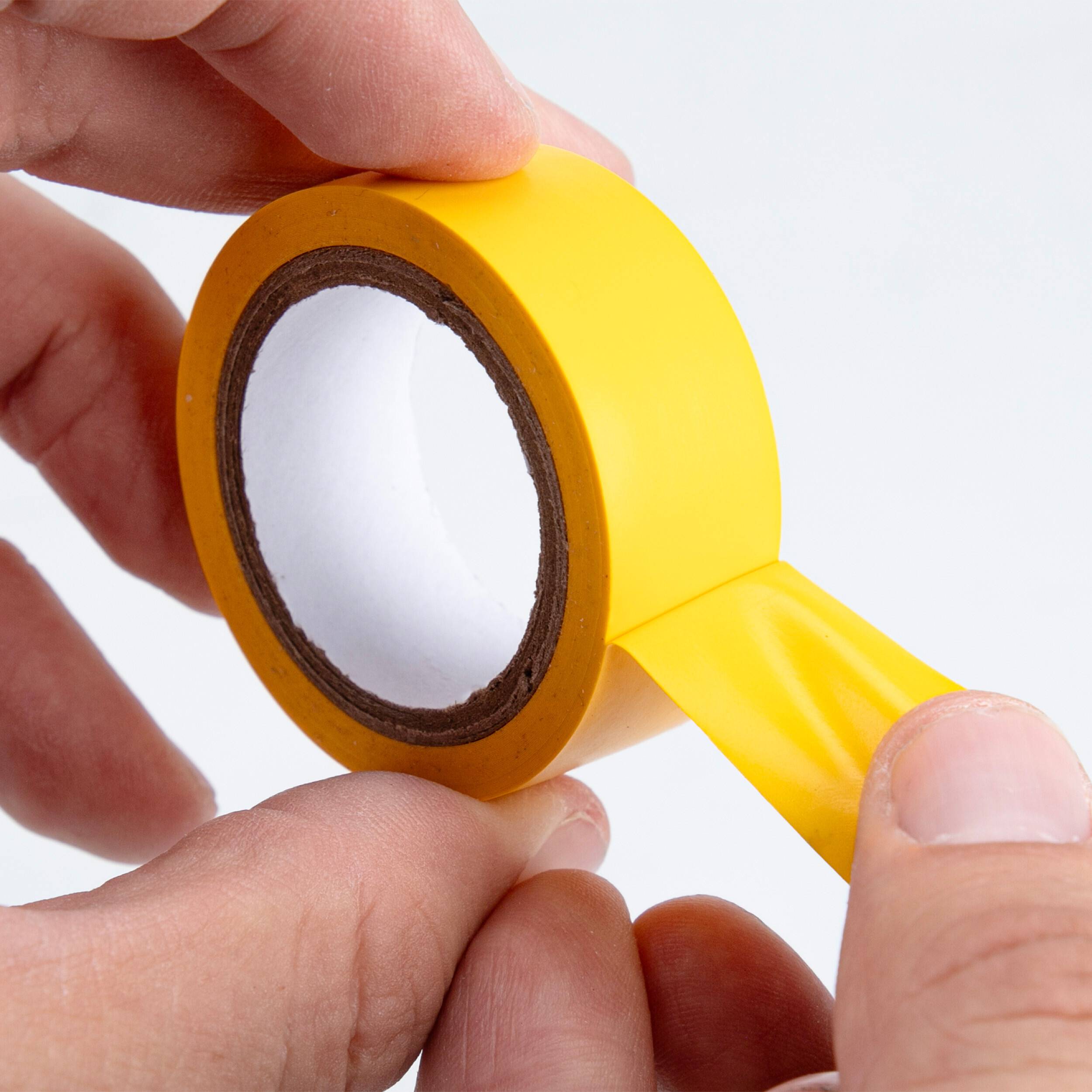 Hände, die ein Stück helles gelbes Klebeband von einer Rolle vor weißem Hintergrund abziehen.