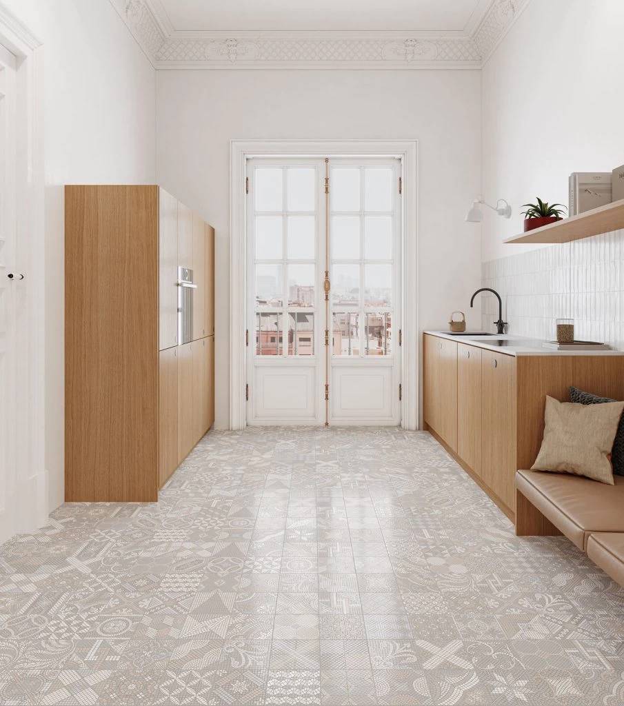Helle moderne Küche mit hellem Holzschränken, gemusterten Bodenfliesen und Glastüren, die auf einen Balkon führen.