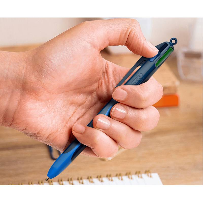 Eine Hand, die einen blau-mehrfarbigen Stift über ein Notizbuch auf einem Holzschreibtisch hält, bereit zum Schreiben.