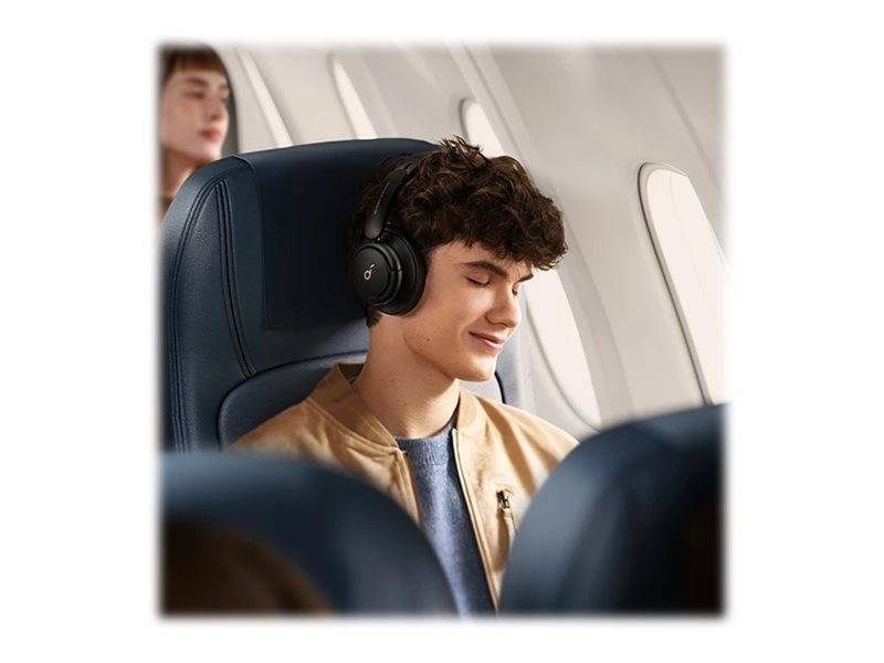 Junger Mann mit Kopfhörern lächelt mit geschlossenen Augen, während er in einem Flugzeug sitzt, mit einem anderen verschwommenen Passagier hinter ihm.