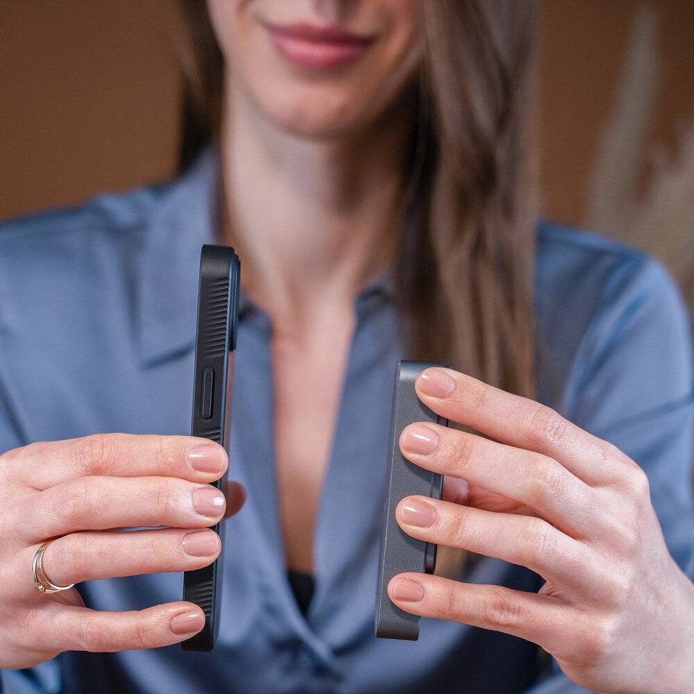 Eine Person hält zwei rechteckige elektronische Geräte in ihren Händen, je eines in jeder Hand, vor einem unscharfen Innenraum-Hintergrund.