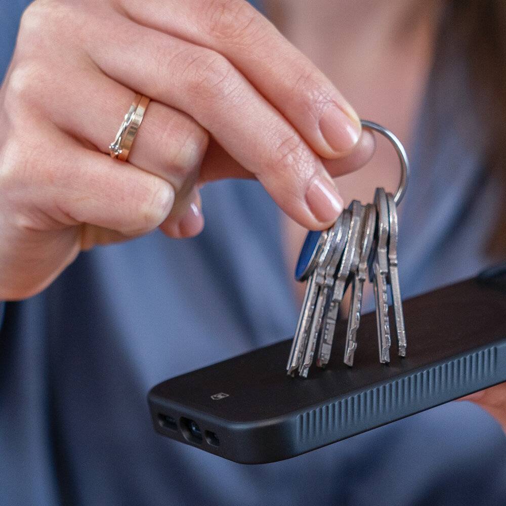 Eine Person hält ein Smartphone mit einem Schlüsselring, der mit einem magnetischen Zubehörteil auf der Rückseite befestigt ist.