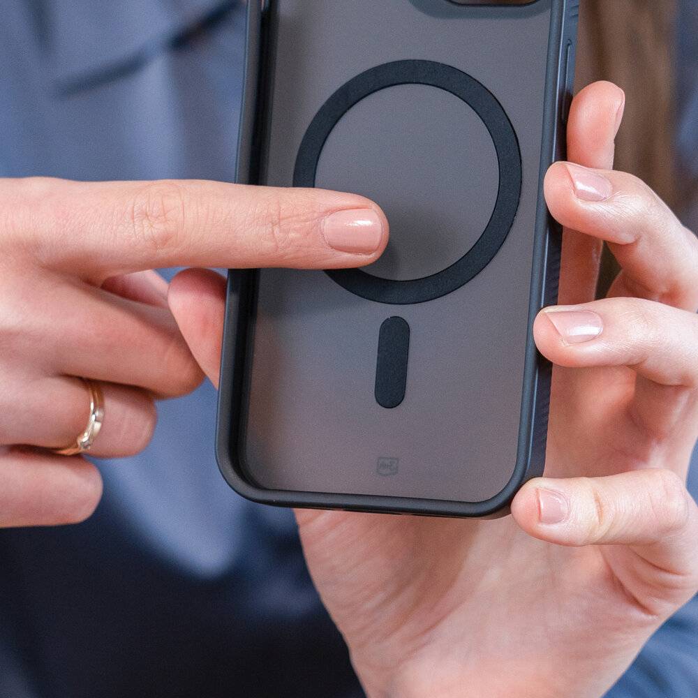 Person hält ein Smartphone mit einem Finger, der auf die Rückseite zeigt, die ein kreisförmiges Design hat, möglicherweise zur Anzeige von kabelloser Aufladung.