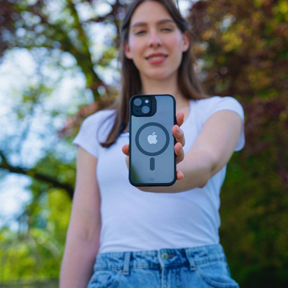 Eine Person, die ein Smartphone mit sichtbarem Apple-Logo auf der Rückseite hält, im Freien bei sonnigem Wetter mit Bäumen im Hintergrund.