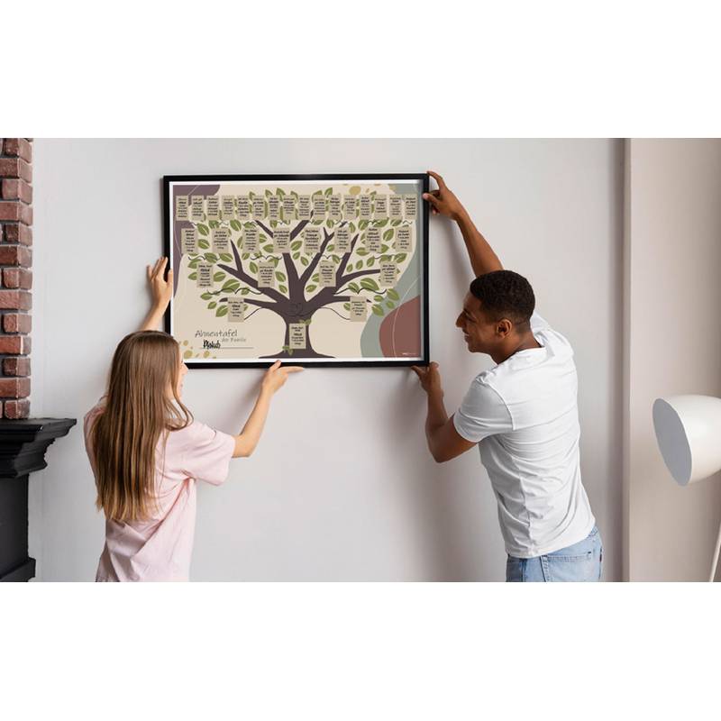Ein Mann und eine Frau hängen einen gerahmten Stammbaum an die Wand in einem Wohnzimmer und arbeiten zusammen, um ihn gerade auszurichten.
