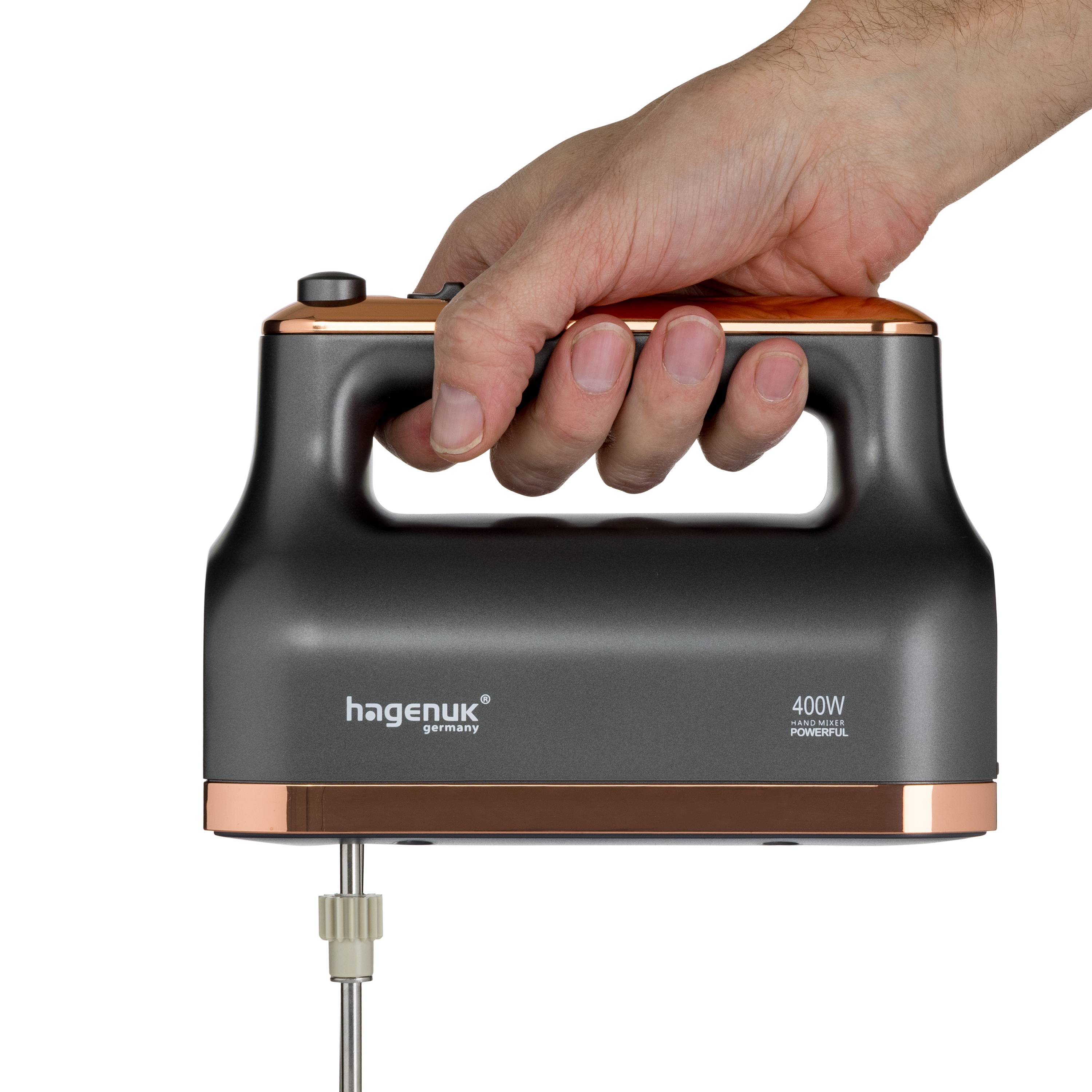 Eine Hand hält einen schwarzen Handmixer mit Kupferakzenten, auf dem der Markenname „hagenuk