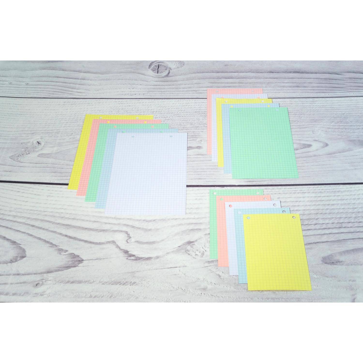 Drei Stapel von Pastellgraph-Papier-Notizkarten auf einer hellbraunen Holzoberfläche angeordnet, mit sichtbaren weißen, grünen, gelben, rosa und blauen Blättern.