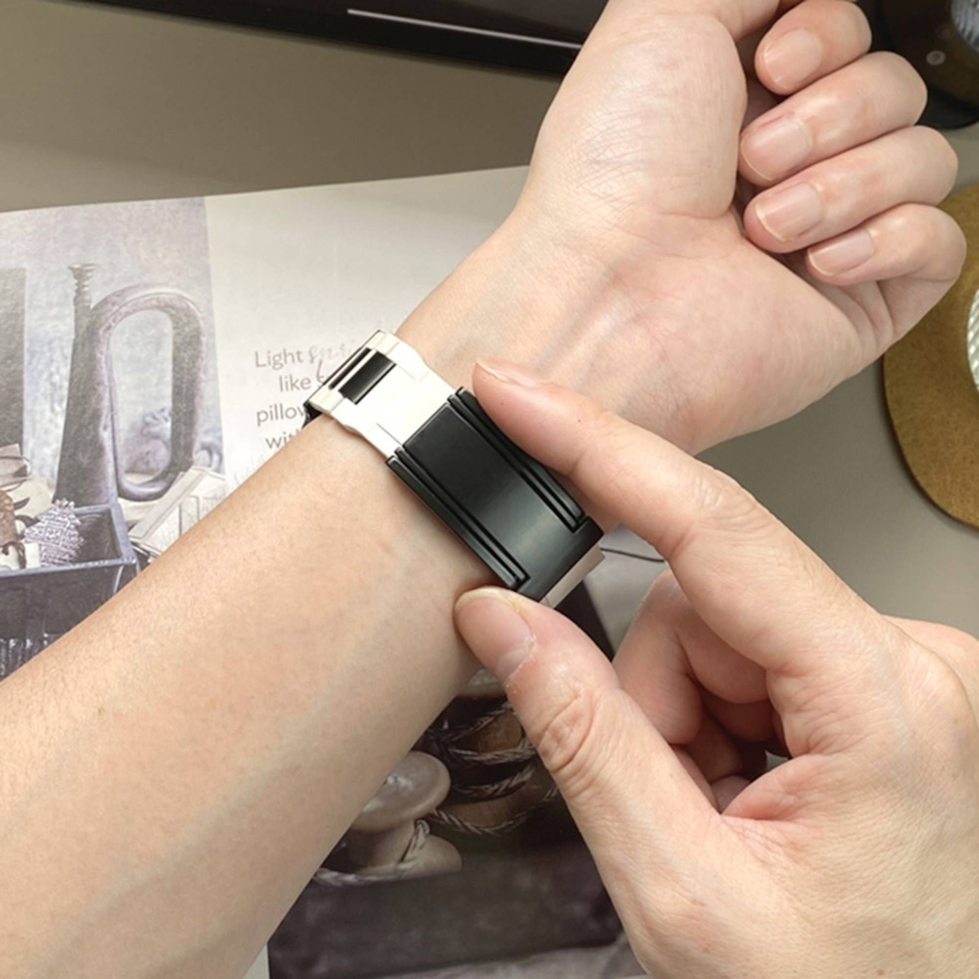 Nahaufnahme eines Handgelenks, das einen schwarzsilbernen Fitness-Tracker trägt, wobei eine Hand die Bandschließe verstellt.