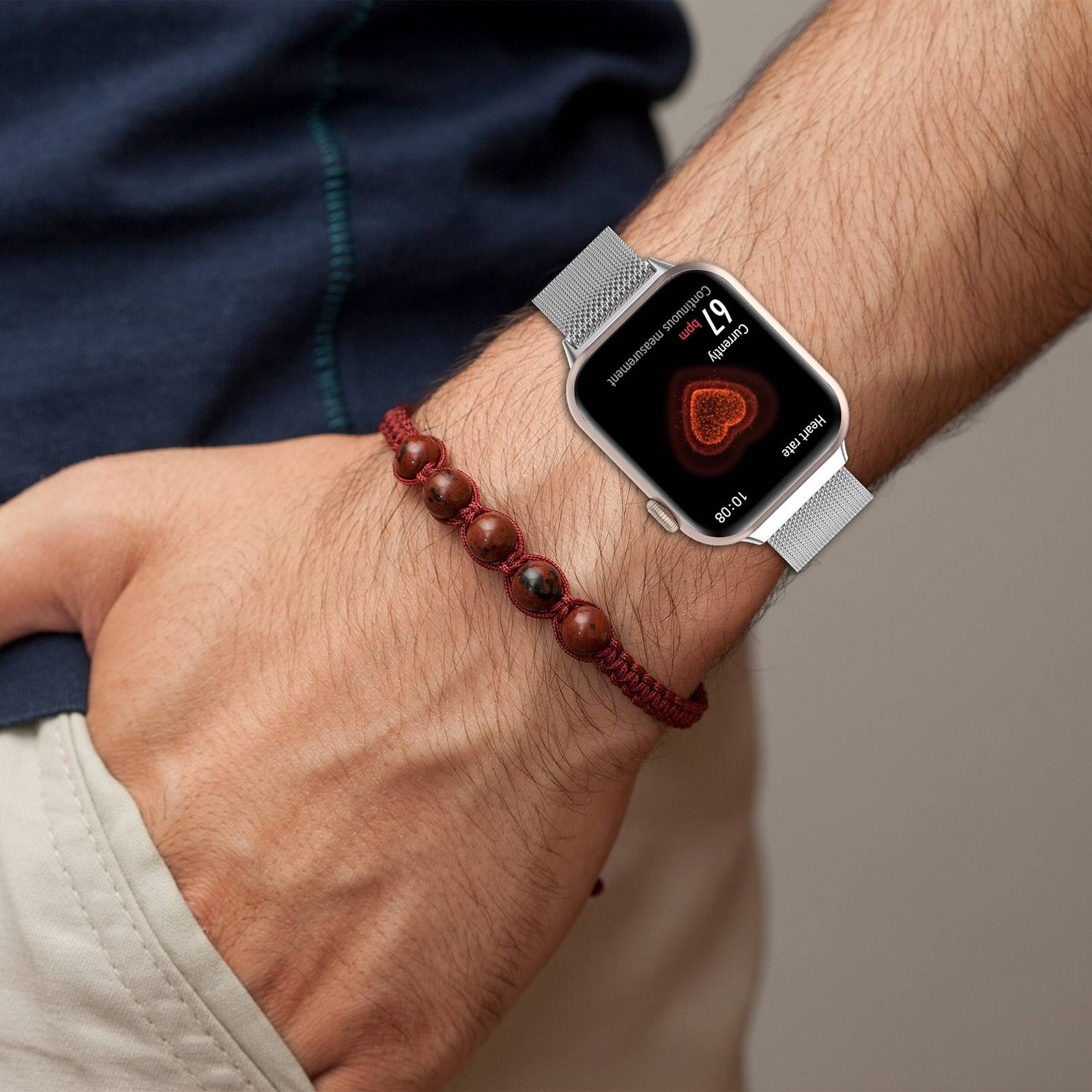 Nahaufnahme eines Handgelenks mit einer silbernen Smartwatch mit Herzfrequenz-/Gesundheitsanzeige und einem braunen Perlenarmband.