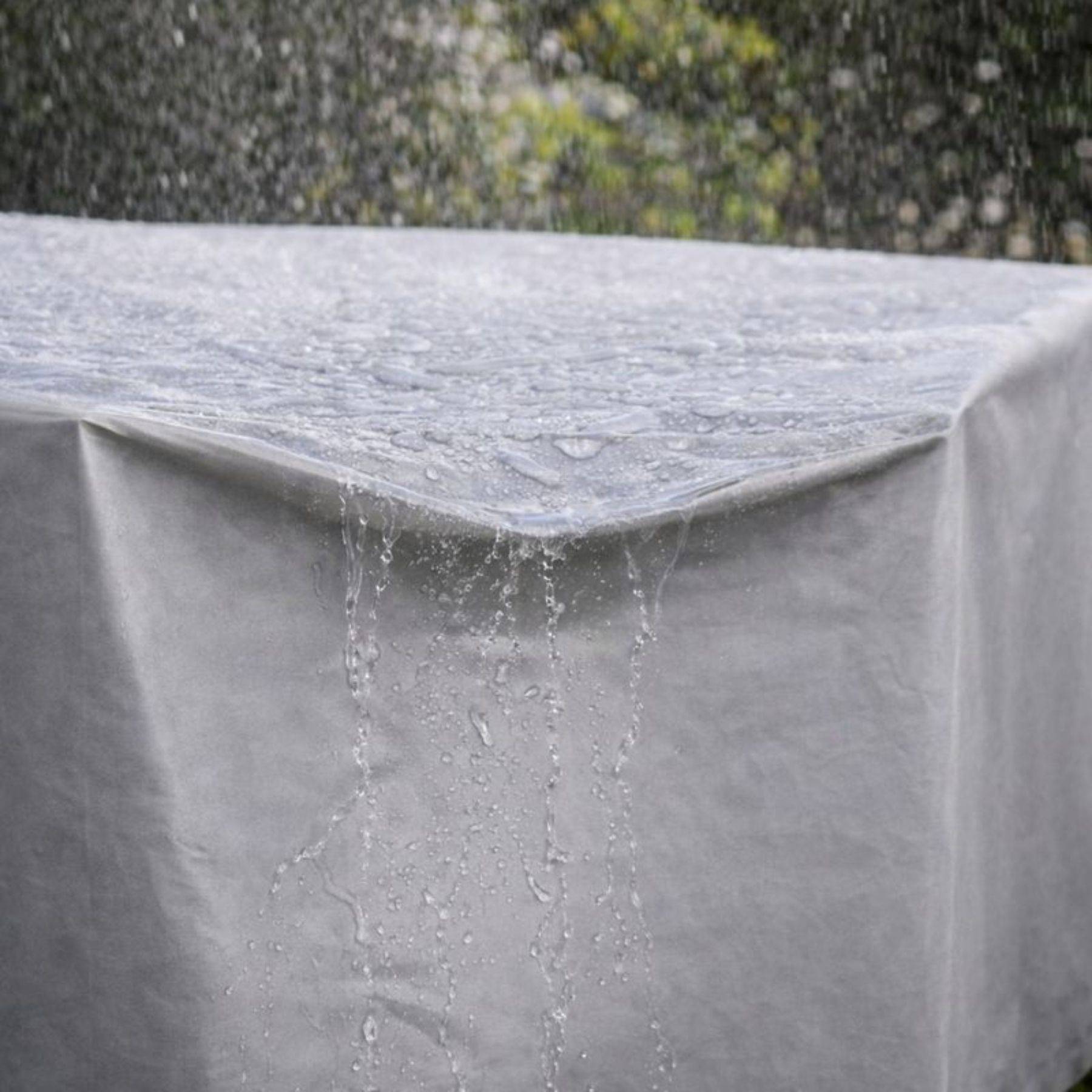 Eine Nahaufnahme von Regenwasser, das von der Ecke einer wasserdichten, grauen Schutzhülle für Gartenmöbel abfließt, die ihre Wirksamkeit demonstriert.