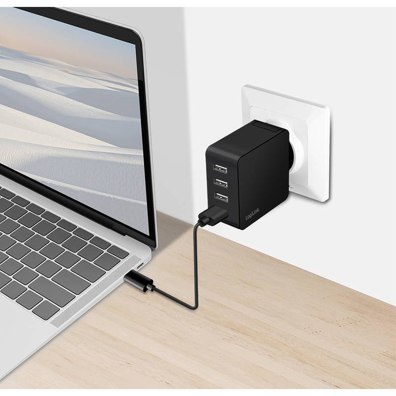 Ein Laptop ist an ein schwarzes Wandladegerät mit drei USB-Anschlüssen angeschlossen, der in eine Steckdose an einem hellen Holzschreibtisch gesteckt ist und damit das Laden anzeigt.