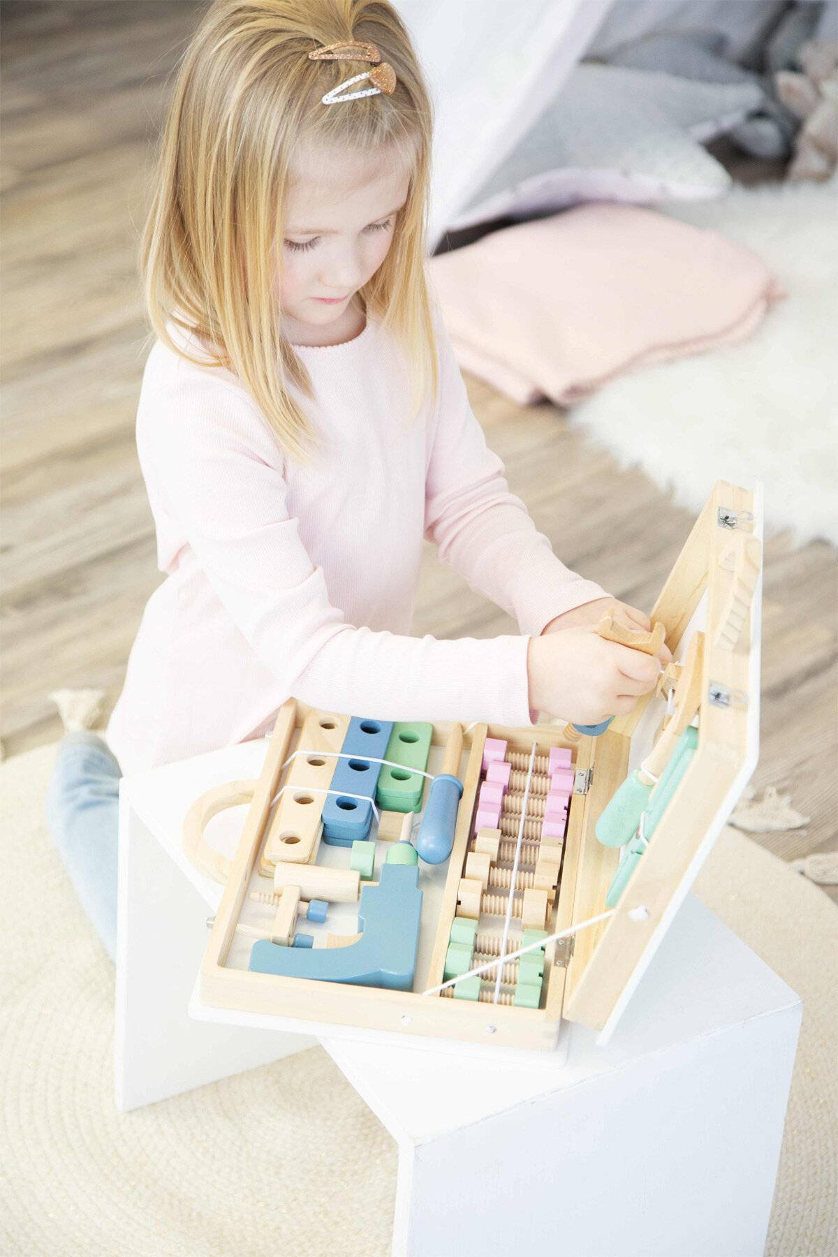 Ein Kind beschäftigt sich mit einem Holzaktivitätsbrett mit Zahnrädern, Hebeln und bunten Bausteinen, das die Feinmotorik und Kreativität fördert.