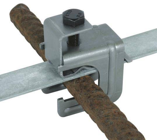 Eine Metallklemme sichert eine rostige Bewehrungsstange an einem flachen Metallstreifen und zeigt eine Verbindung zwischen zwei verschiedenen Metallkomponenten.